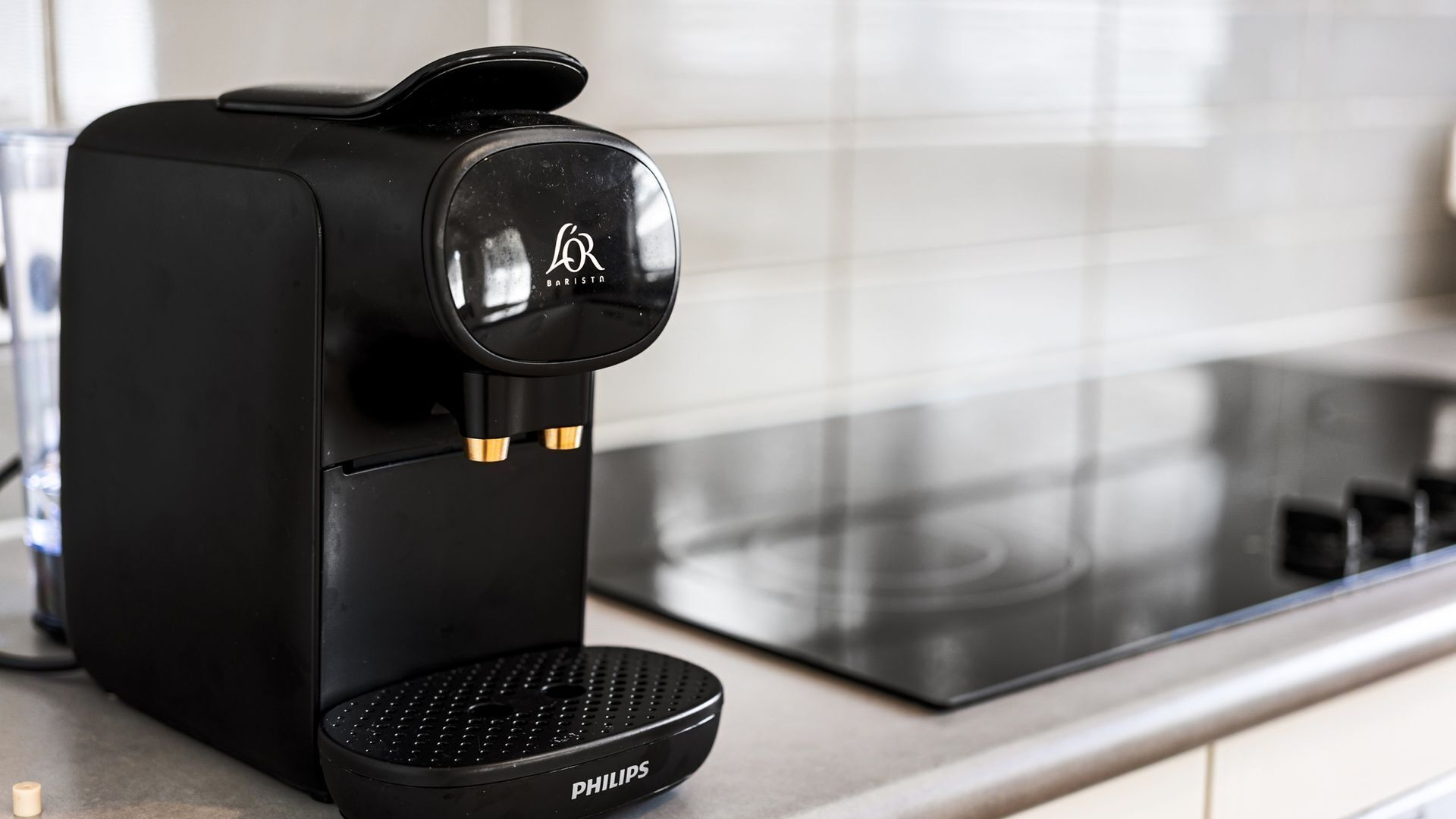 A black coffee machine with a brand logo, two coffee pods, and a water reservoir on a kitchen counter.