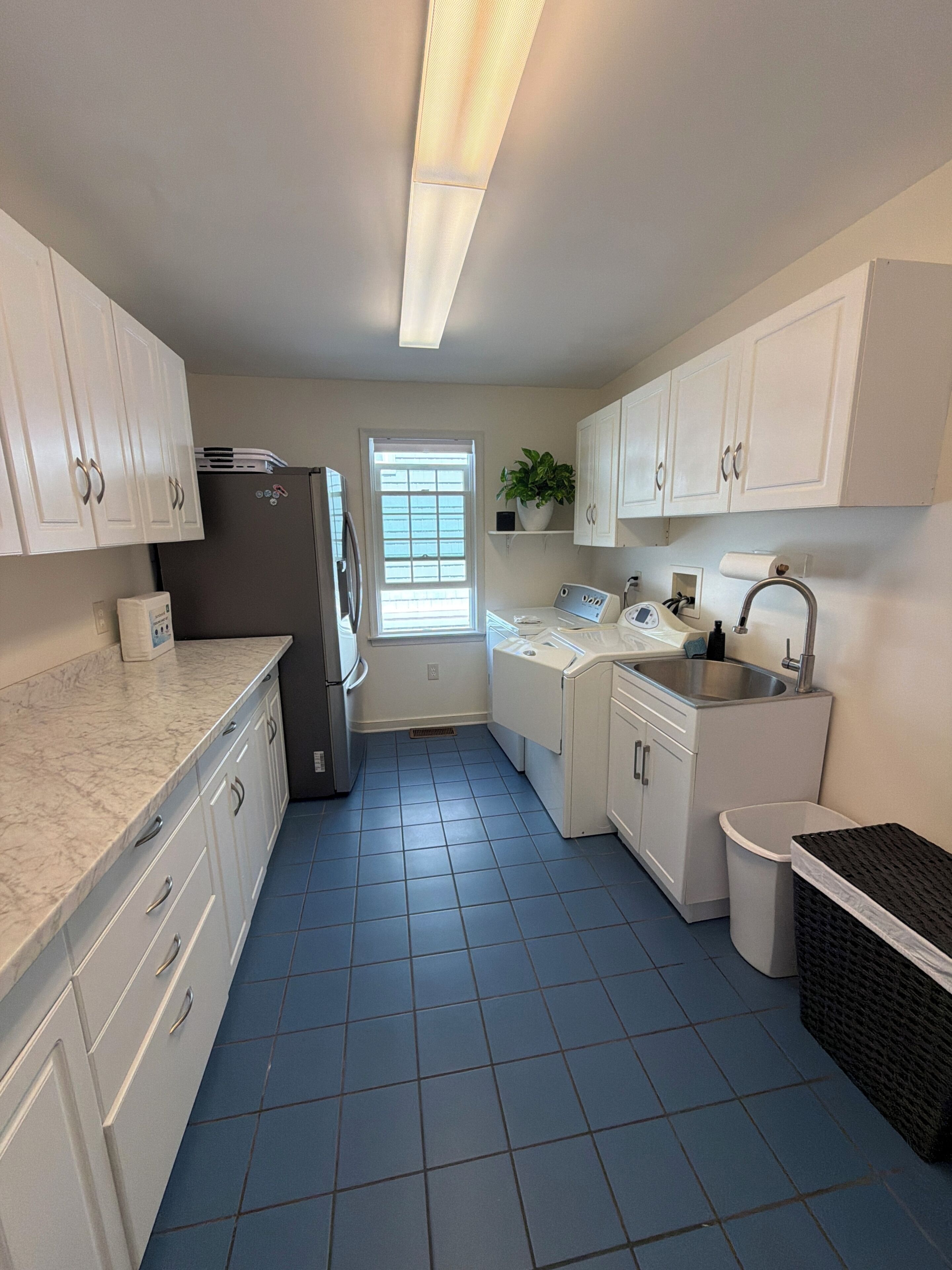 A compact kitchen with white cabinets, a refrigerator, a washing machine, a sink, and a window with blinds.
