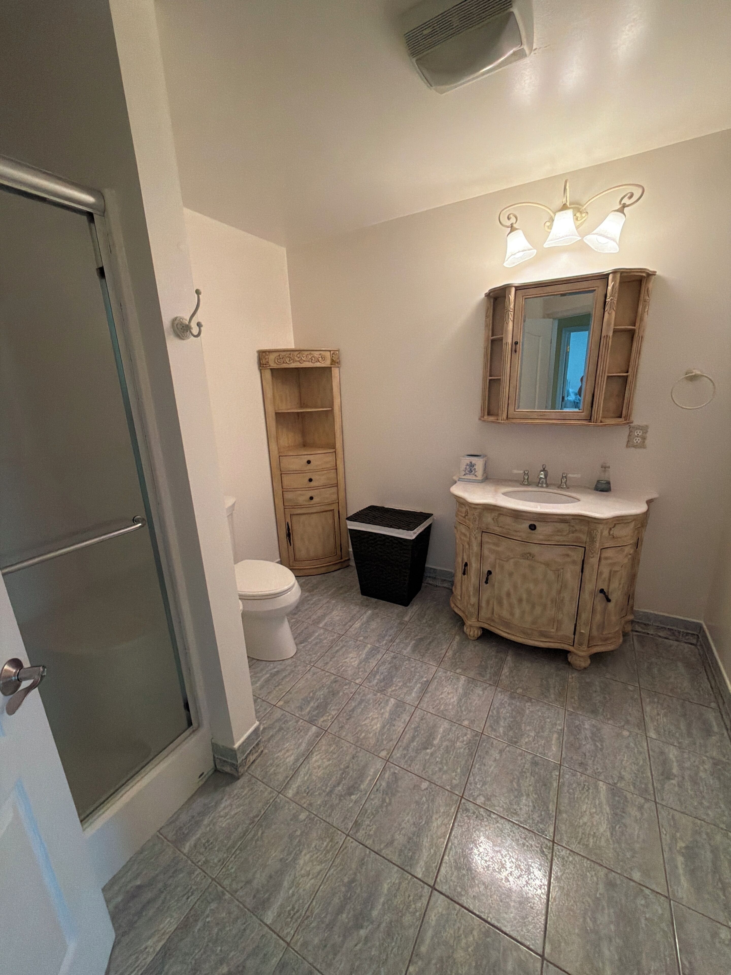 Een badkamer met toilet, wastafel met spiegel en prullenbak.