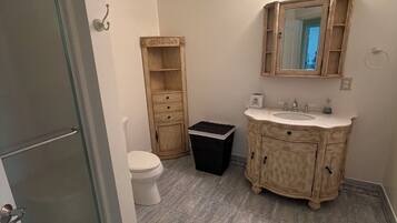 Een badkamer met toilet, wastafel met spiegel en prullenbak.