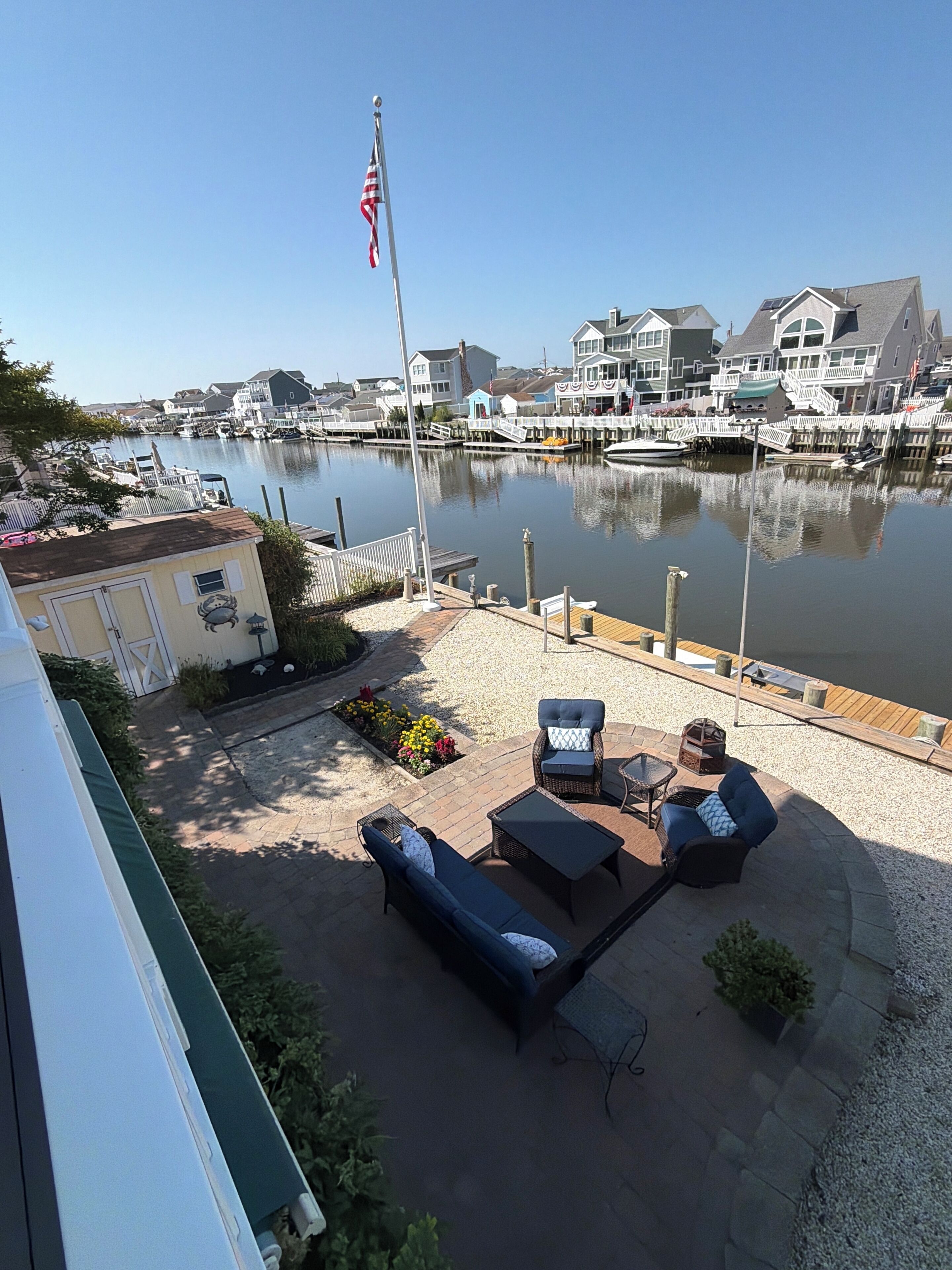 A waterfront patio with outdoor furniture, a flag, and a marina in the background.