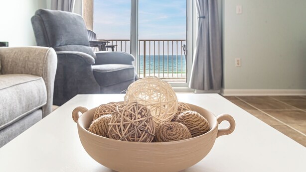 Quarto com vista para o mar, um sofá, uma mesa com uma tigela de objetos decorativos e uma cadeira.