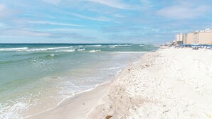 Uma praia com céu claro, ondas e edifícios ao longo da costa.