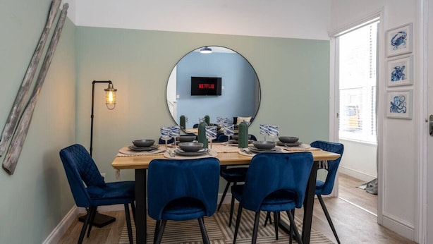 Un coin repas agrémenté d’un miroir rond, d’un téléviseur à écran plat et de chaises bleues.