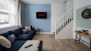 Un salon avec un mur bleu, un téléviseur fixé au mur qui affiche le logo « NETFLIX », un escalier et un jeu de fléchettes.