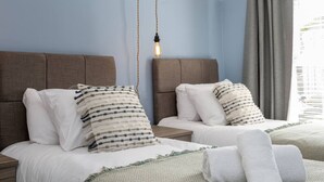 Une chambre d’hôtel avec deux lits, chacun doté d’une tête de lit, de draps blancs et d’oreillers à rayures. Un luminaire suspendu se trouve au-dessus des lits.