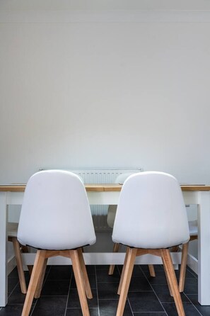 Ein Zimmer mit einem weißen Schreibtisch und zwei weißen Stühlen mit Holzbeinen.