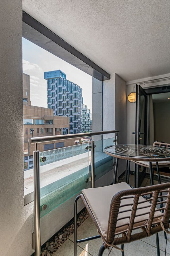 Ein Balkon mit Glasgeländer, einem runden Tisch und zwei Korbstühlen.
