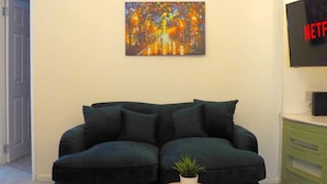 A living room with a dark green sofa, a painting on the wall, a small table with a plant, and a TV mounted on the wall. - 4 Bed • Parking • Close to M4 – Ideal for Work (Neath Port Talbot Principle Area)