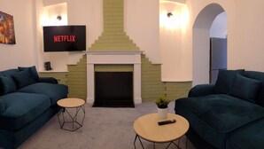 A living room with two sofas, a fireplace, a TV displaying 'NETFLIX', and a small table with a remote control. - 4 Bed • Parking • Close to M4 – Ideal for Work (Neath Port Talbot Principle Area)
