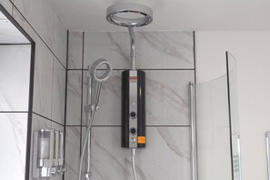 Um chuveiro moderno com chuveiro manual, painel de controle na parede e box de vidro.