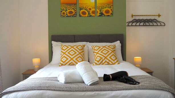 A neatly made bed with patterned pillows, a bedside lamp, and a wall-mounted coat rack. - 4 Bed • Parking • Close to M4 – Ideal for Work (Neath Port Talbot Principle Area)