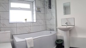 A modern bathroom with a bathtub, toilet, and sink, featuring marble tiles and a window. - 4 Bed • Parking • Close to M4 – Ideal for Work (Neath Port Talbot Principle Area)