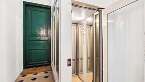 Un corridoio con una porta verde, un ascensore e un pavimento piastrellato.