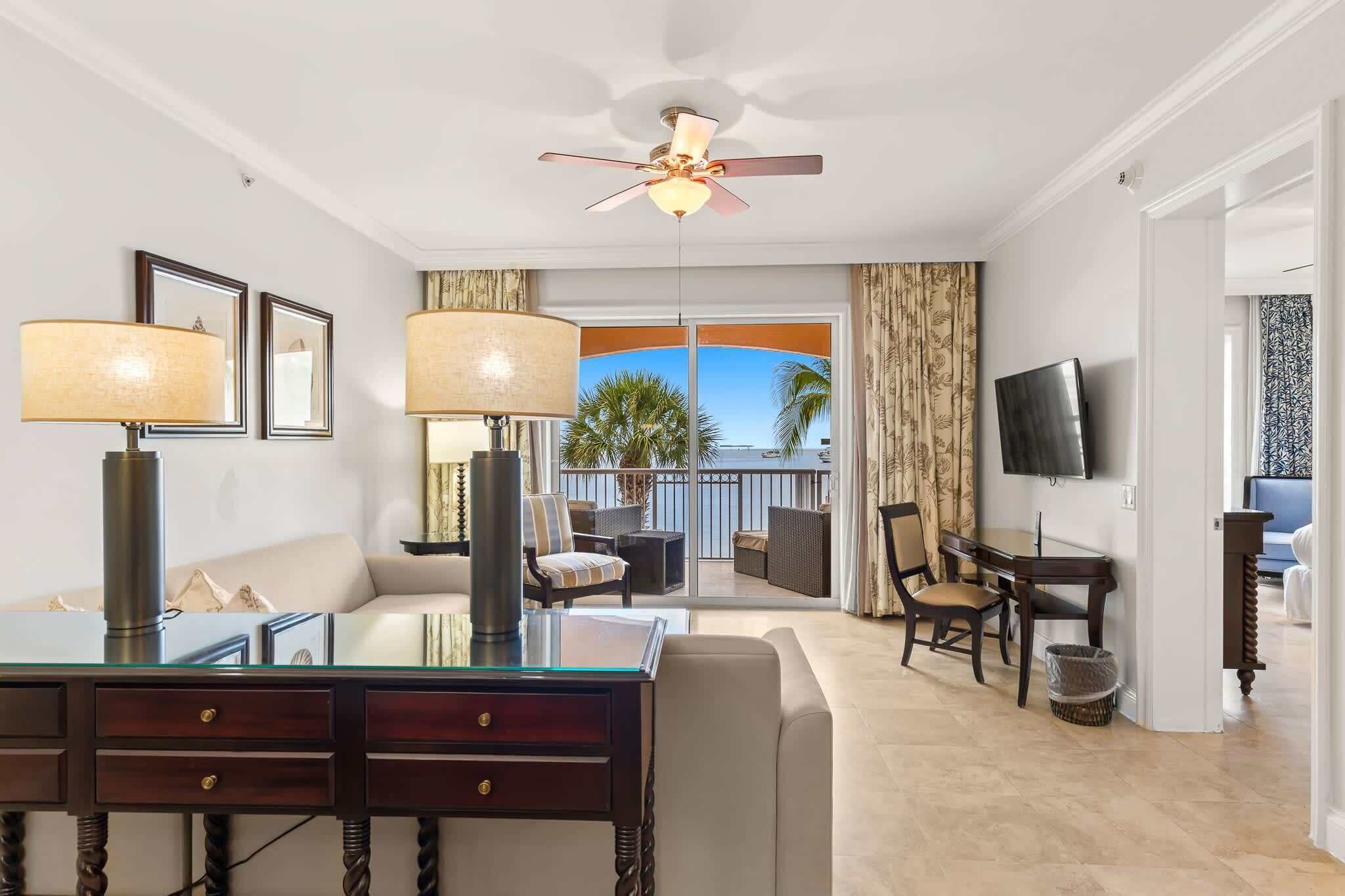 A hotel room with a balcony, a dining area, a TV, and a ceiling fan.