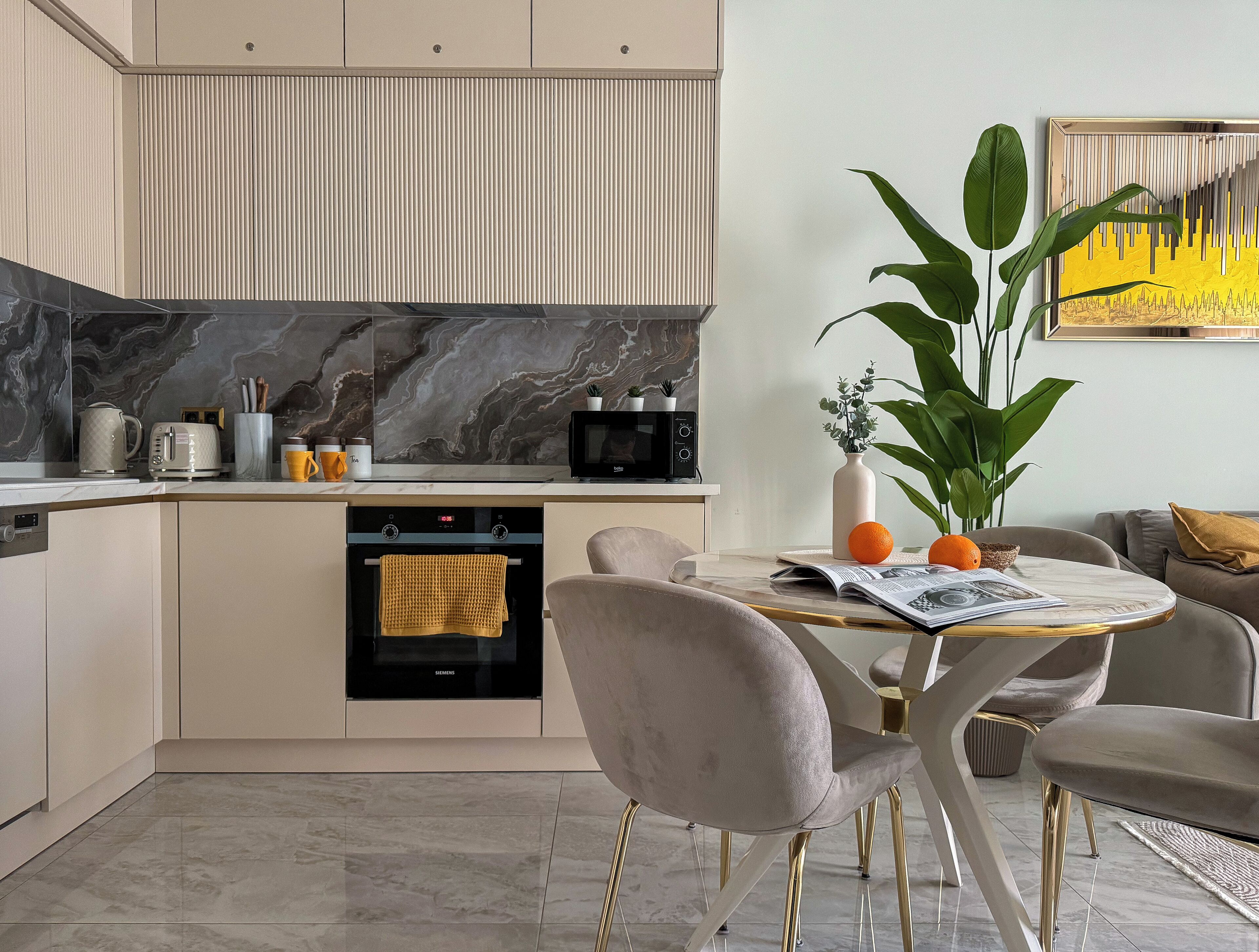 A modern kitchen with a built-in oven, a microwave, and a coffee maker. There is a dining table with chairs and a plant on the table.