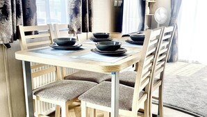A dining area with a wooden table and chairs, a fan, and a TV. - Elegant 2 Bed One and Half Bath Caravan (Northampton)