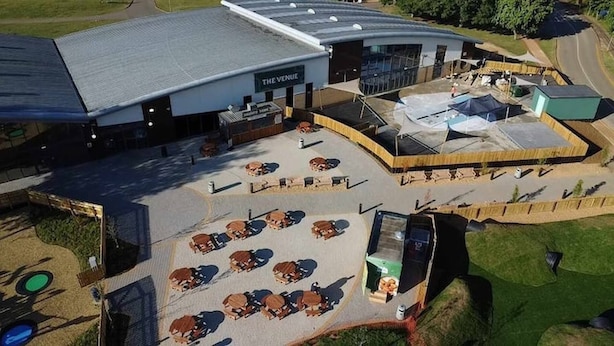 A building with a sign reading 'THE VENUE' and a parking lot with multiple tables and chairs. - Elegant 2 Bed One and Half Bath Caravan (Northampton)