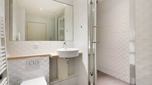 A modern bathroom with a white sink, mirror, and shower. - Bel appartement pour 4 - Palais des Expositions (Paris)