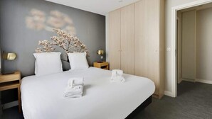 A hotel room with a bed, a nightstand, a lamp, a wardrobe, and a wall-mounted flower arrangement. - Bel appartement pour 4 - Palais des Expositions (Paris)