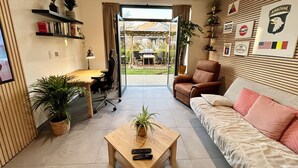Una sala de estar con sofá, mesa de centro, escritorio con silla, televisor y un ventanal grande.