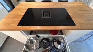Una cocina con encimera de madera, estufa integrada y un cajón con ollas y sartenes.