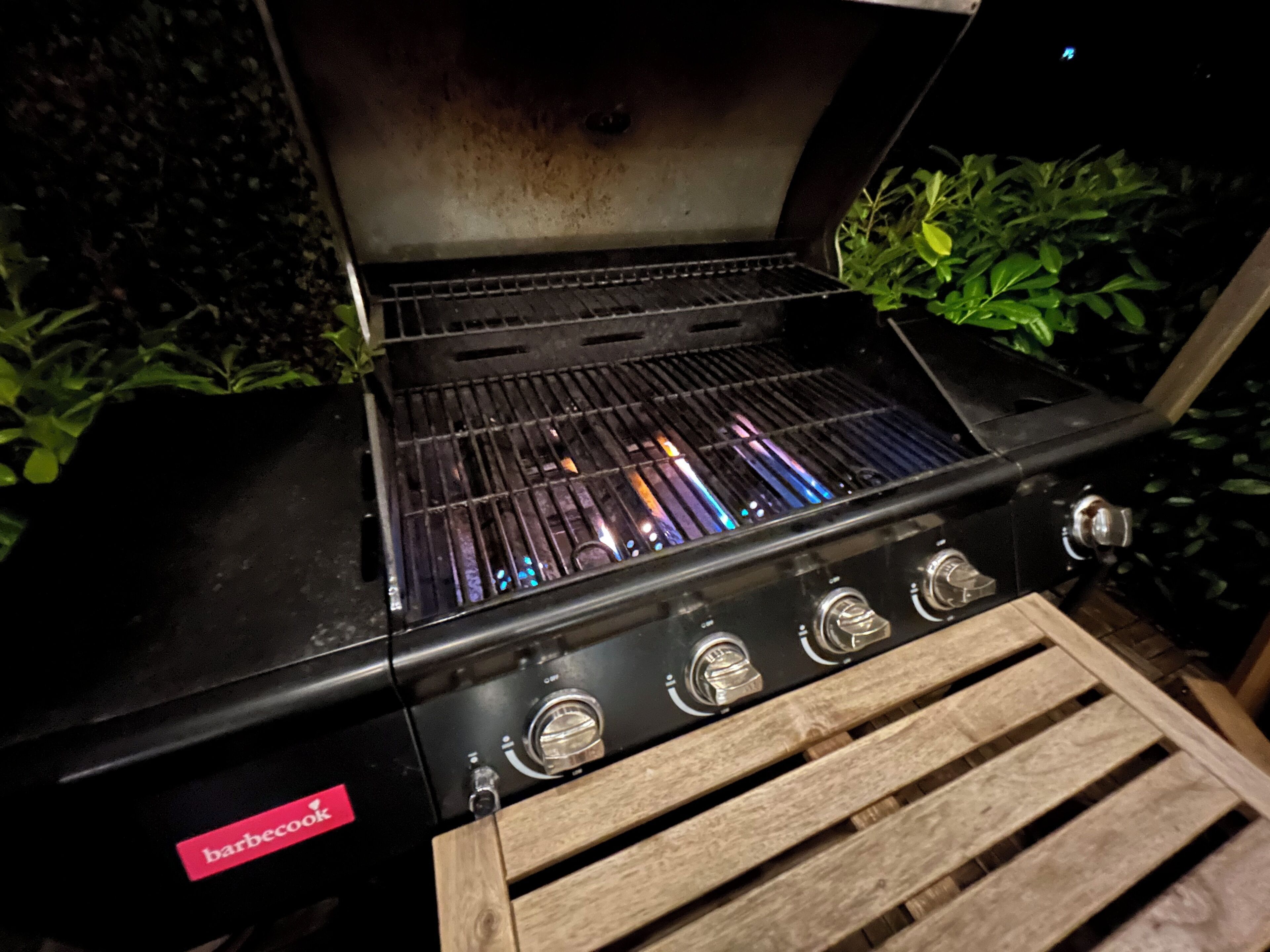 A barbecue grill with a 'barbecook' label, four control knobs, and a grate with visible food residue.