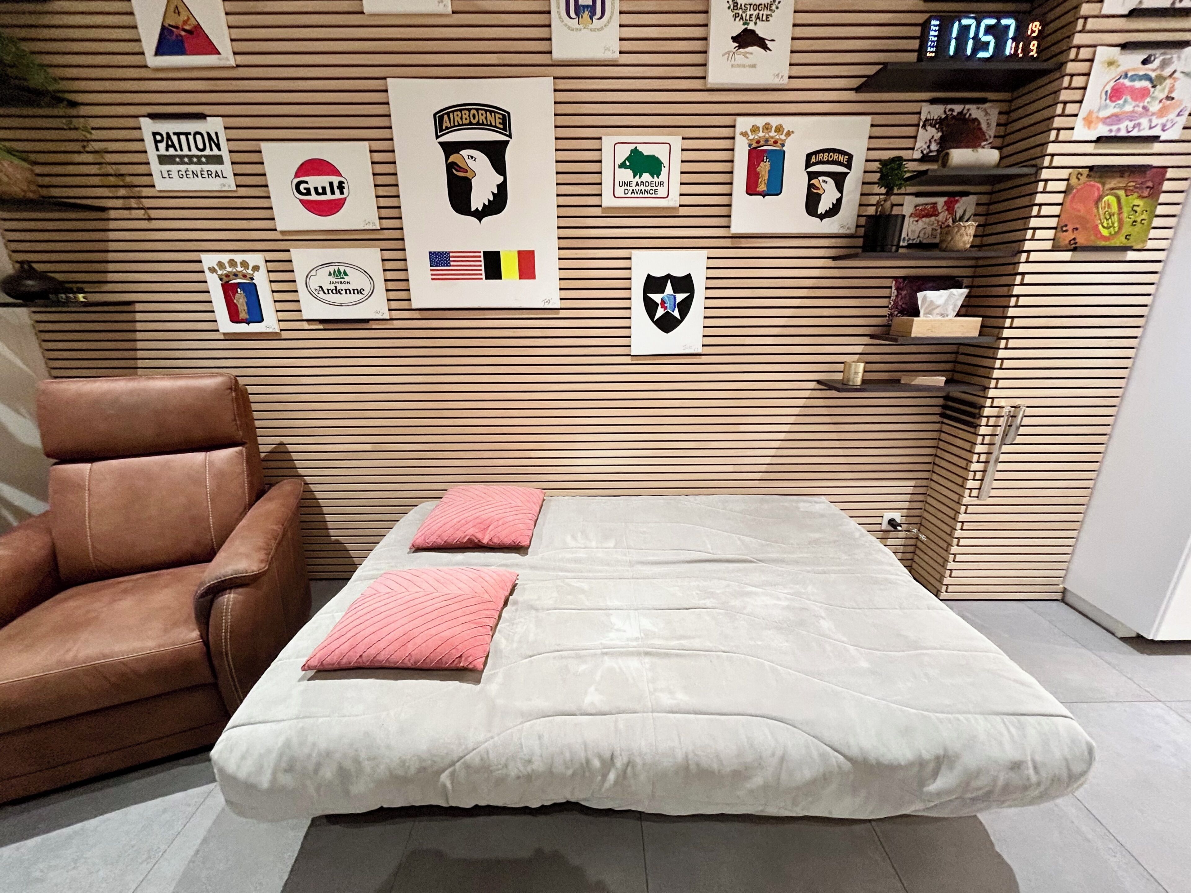 Une pièce comprenant un lit, un fauteuil en cuir marron et divers éléments de décoration murale, notamment des drapeaux et des emblèmes.