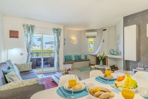 Un salon moderne avec un canapé, une table à manger où sont disposés des aliments pour le petit-déjeuner, et un balcon offrant une vue agréable.
