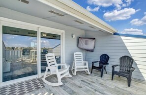 A covered outdoor area with a sliding glass door leading to a patio, two white rocking chairs, and two black chairs. - C 33 Sundown Condominiums (Pensacola)