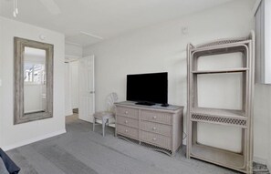 Ein Zimmer mit Fernseher auf einer Kommode, einem Sessel und einem großen Spiegel an der Wand.