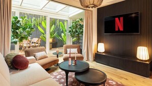 Ein modernes Wohnzimmer mit Flachbildfernseher, bequemen Sitzgelegenheiten und einem großen Fenster mit Pflanzen.