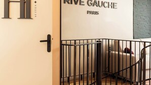 Ein Hotel Eingang mit einer weißen Tür, die ein großes 'H' trägt, einer Treppe mit Metallgeländer und einem Schild, das 'RIVE GAUCHE PARIS' zeigt.