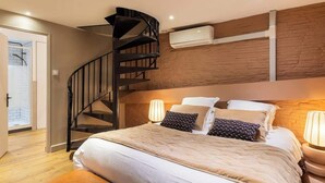 Ein Schlafzimmer mit einem Bett, zwei Nachttischlampen, einem Holz-Kopfteil, einer Wendeltreppe und einer Klimaanlage.
