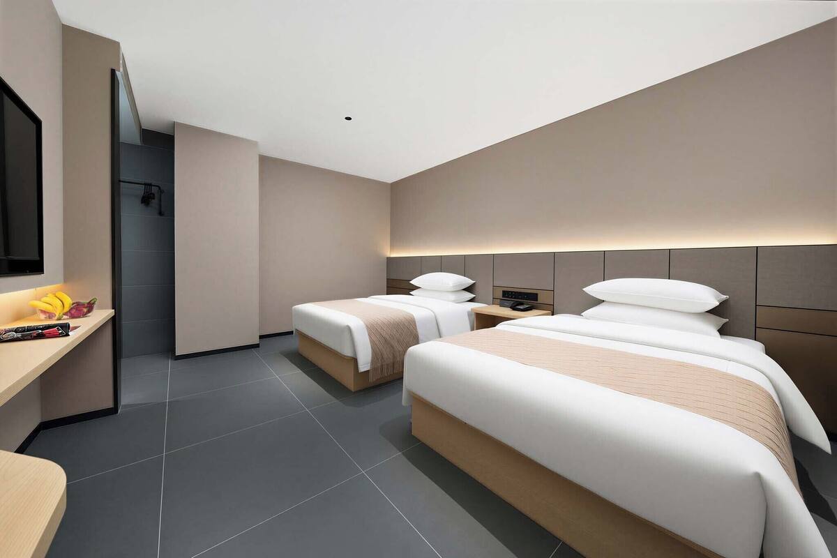 Una habitación de hotel moderna con dos camas, una mesita de noche, un televisor y una zona de ducha.