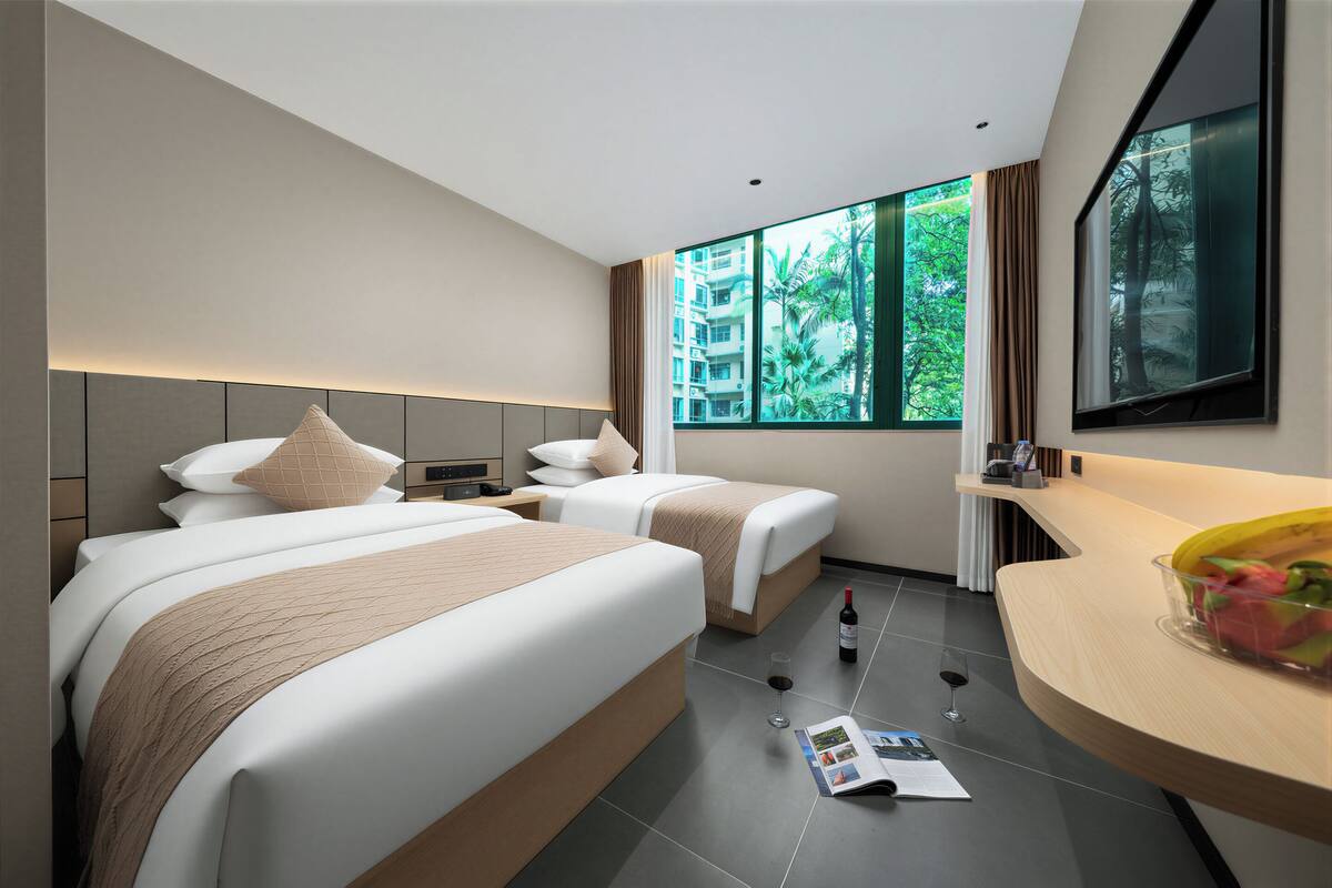 Habitación de hotel moderna con dos camas, un ventanal con vistas a zonas verdes, un escritorio de madera y un espejo.