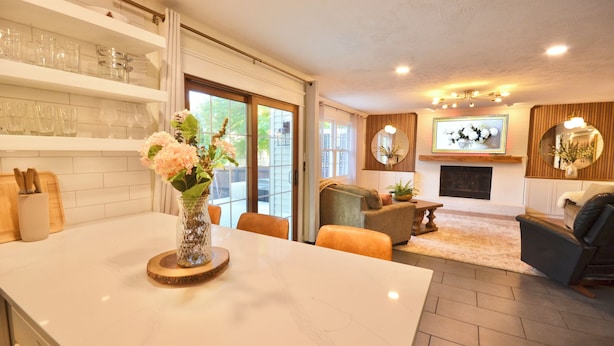 A modern kitchen with a marble countertop, a dining area with a table and chairs, and a living room with a fireplace and seating.