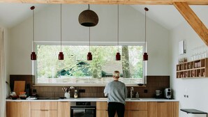 Een moderne keuken met houten kastjes, een groot raam en hangende pendantlampen.