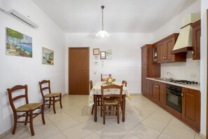 A kitchen with wooden cabinets, a dining table with chairs, and a hanging light fixture. - Apartment 'Giallo' with Terrace, Wi-Fi and Air Conditioning (San Vito Lo Capo)