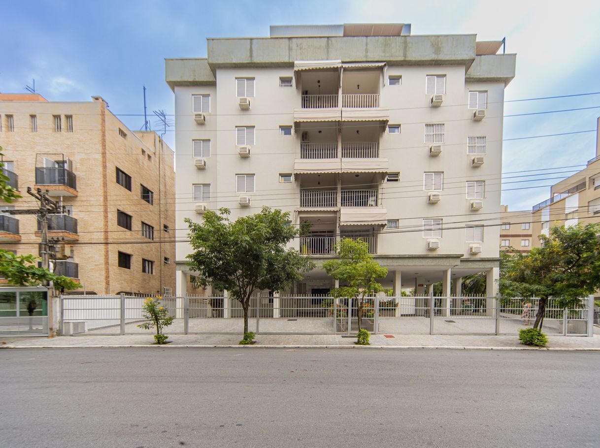 A multi-story building with balconies, a gated entrance, and a clear sky.