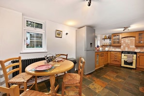 A kitchen with a dining table, chairs, a refrigerator, a stove, and wooden cabinets.