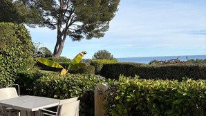 Eine Terrasse im Freien mit Tisch und Stühlen, umgeben von viel Grün und Blick auf das Meer.