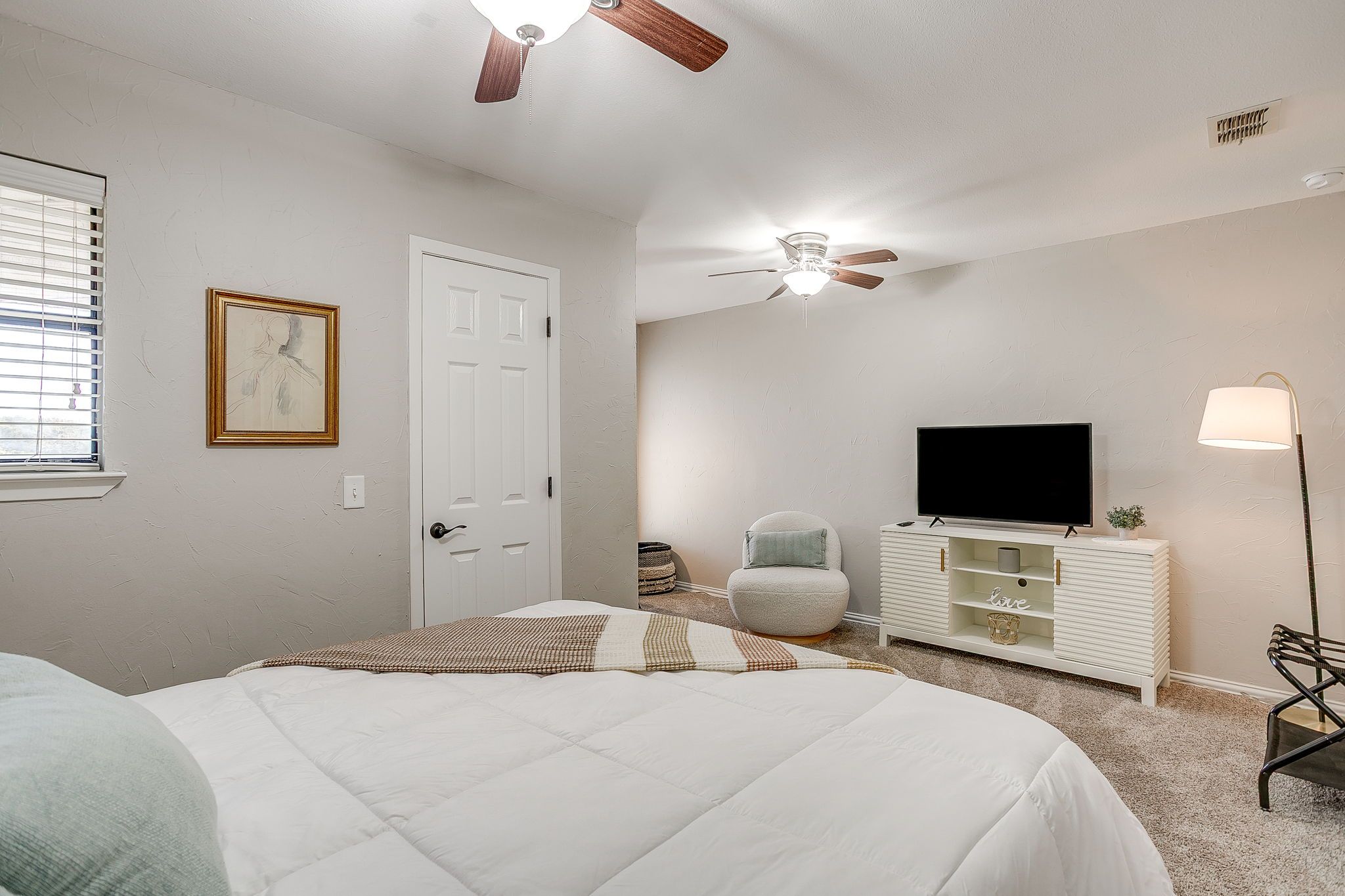 A bedroom with a bed, a ceiling fan, a TV, a bedside lamp, and a door.
