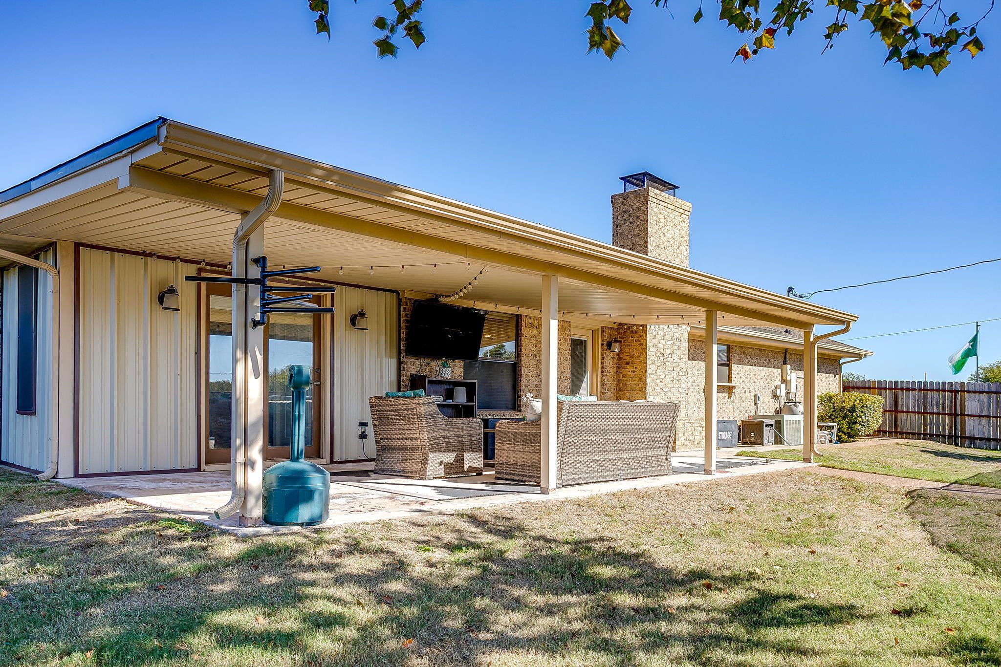 A covered patio area with outdoor furniture, a grill, and a stone chimney.