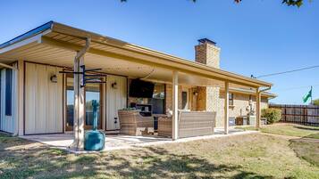 A covered patio area with outdoor furniture, a grill, and a stone chimney.