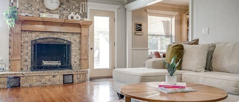 A living room with a stone fireplace, a round coffee table with books, a beige sofa, and a white rug.