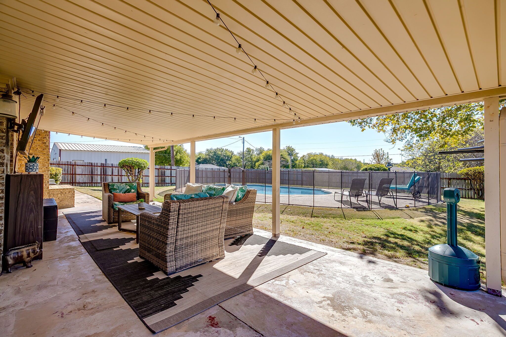 Un patio couvert avec mobilier d’extérieur, une piscine et un jardin clôturé.