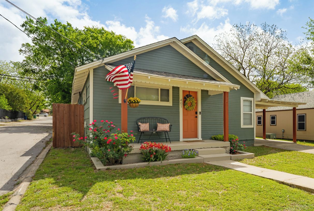 A single-story house with a porch, a front door, and a small garden with flowers.