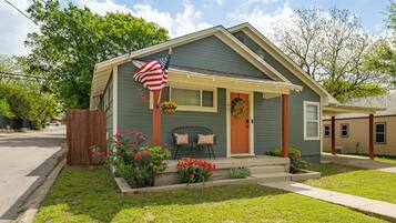 A single-story house with a porch, a front door, and a small garden with flowers.