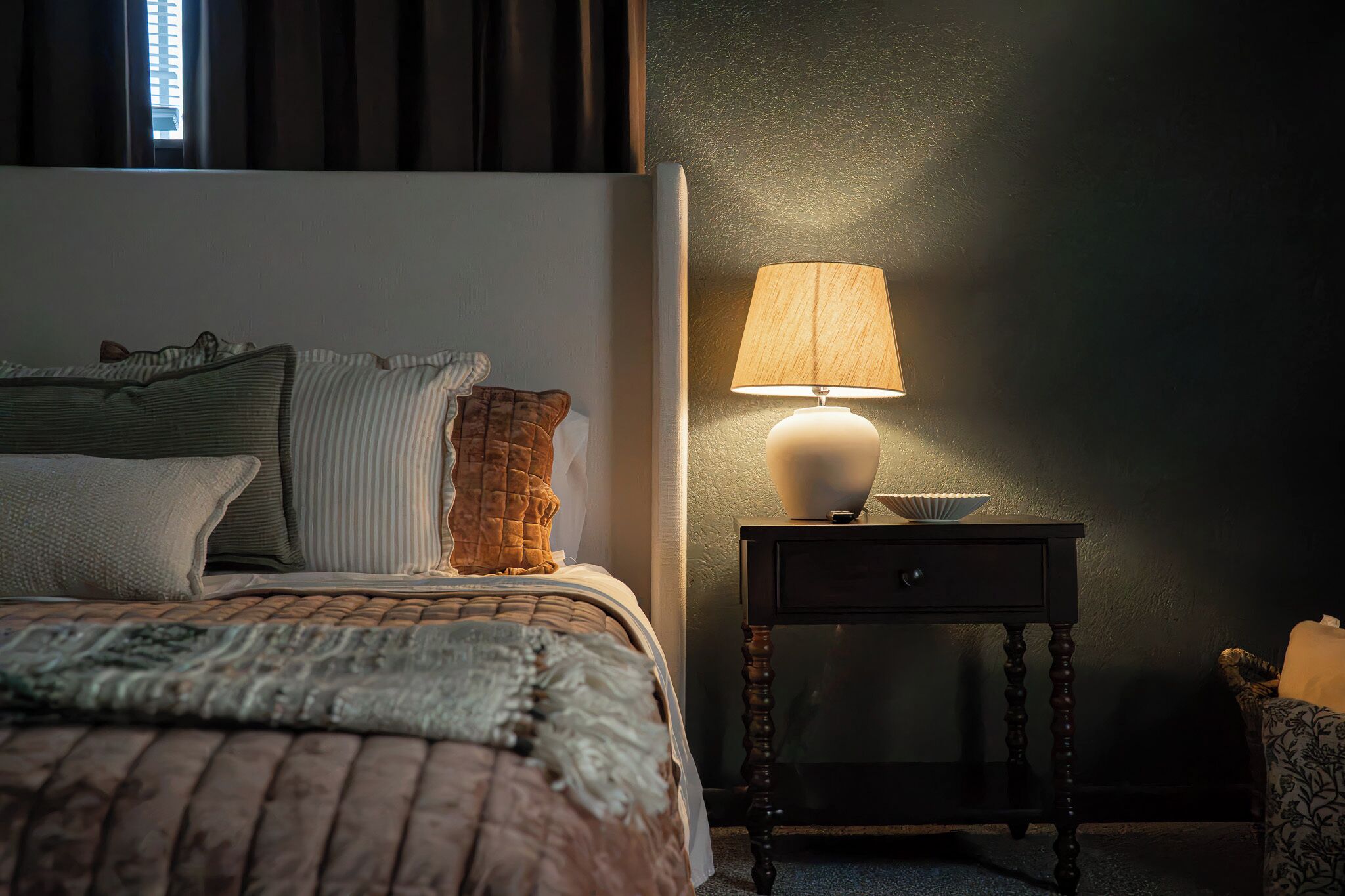 A bedroom with a bed, pillows, a bedside table with a lamp, and a nightstand.